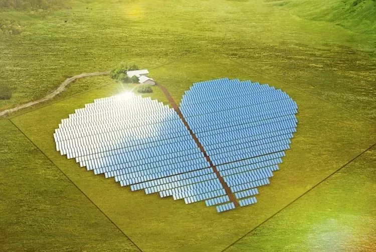 Vista aérea de um conjunto de painéis de energia solar em formato de coração, durante a luz do dia, em meio a um vasto gramado.
