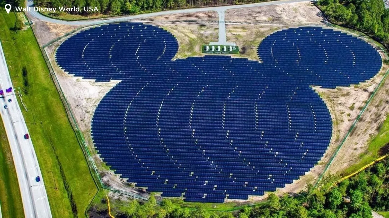 Vista aérea de um conjunto de painéis de energia solar em formato de um círculo grande, junto a dois círculos menores, em meio a um ambiente arborizado, representando o personagem Mickey Mouse.
