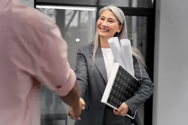 Imagem de uma mulher vestindo roupas sociais e cumprimentando alguém com uma mão, enquanto com a outra, segura duas cartolinas de papel e um protótipo de painel solar mostrando um exemplo de dica de empreendedorismo sustentável.