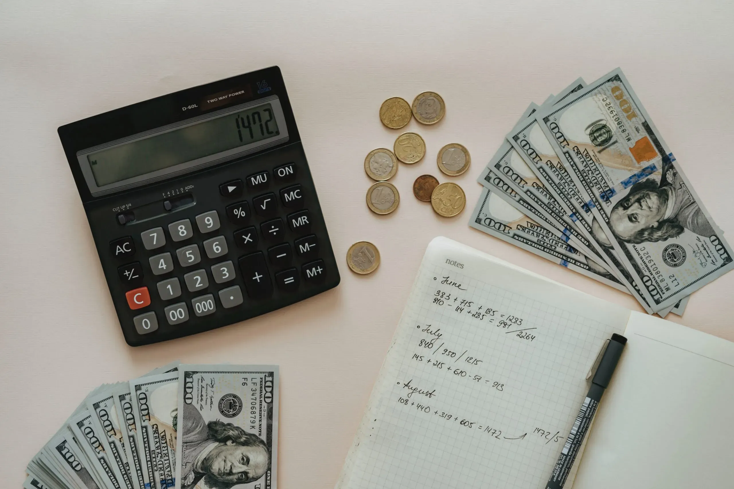 Tecnologias sustentáveis também se relacionam com economia, por isso, a imagem mostra uma calculadora, notas de dinheiro, algumas moedas, uma caneta e um caderno aberto com algumas anotações.