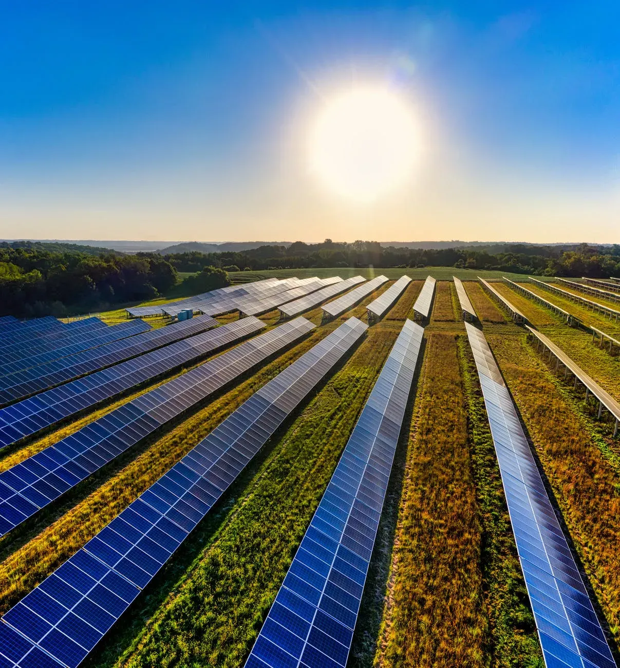 Vista aérea de painéis de energia solar, que é um exemplo de energias verdes, localizado em ambiente externo, durante o dia, em meio a um gramado.