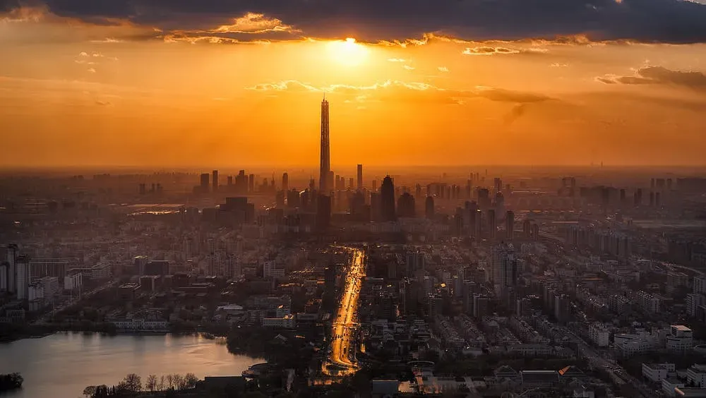 Imagem vista de cima do nascer do Sol em uma grande cidade com muitas casas, prédios e arranha-céus. 